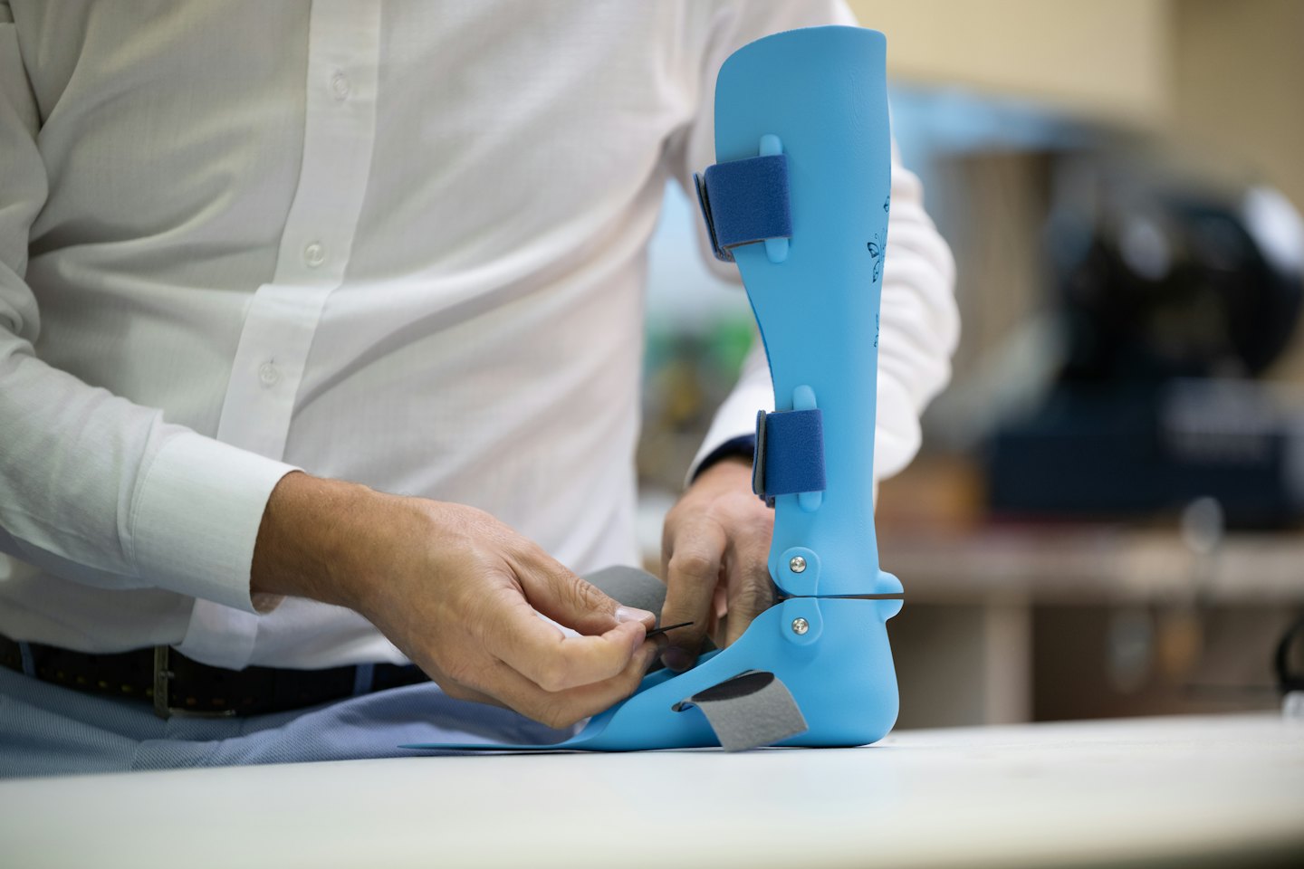 Professional adjusting a light blue ankle-foot brace on a white surface.